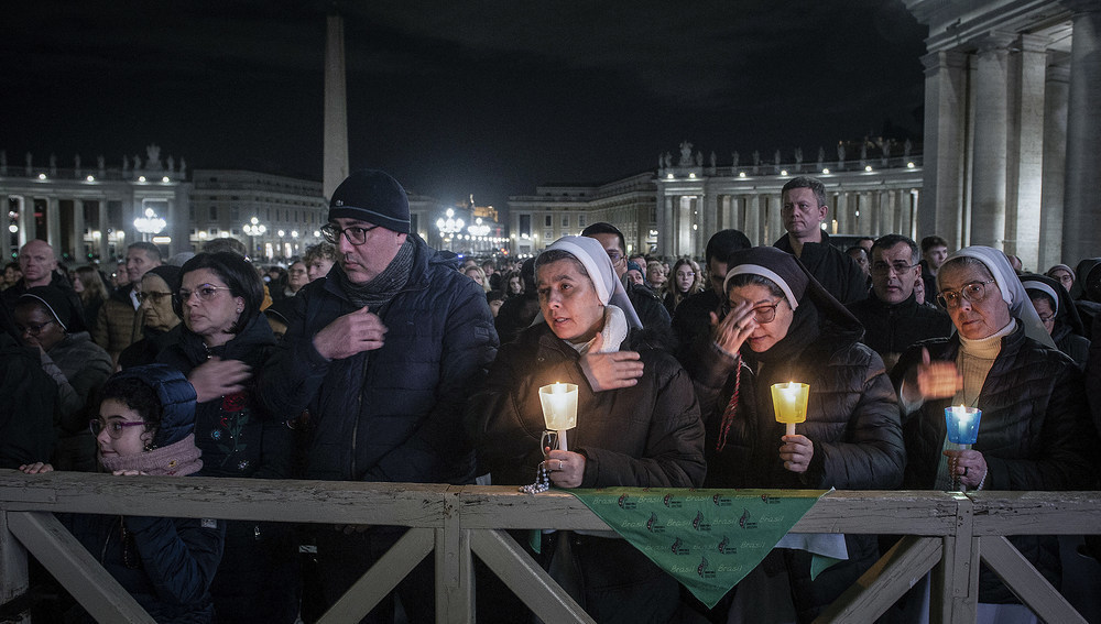 Menschen hinter einer Absperrung darunter Ordensschwestern mit Kerzen, bei einer Rosenkranzandacht für den erkrankten Papst am 28. Februar 2025 auf dem Petersplatz im Vatikan.