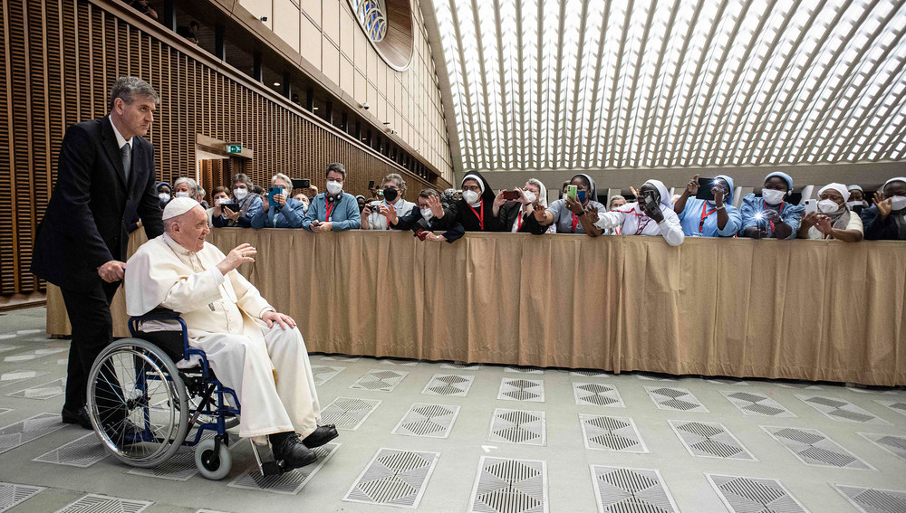 Papst Franziskus sitzt im Rollstuhl und winkt lachend Teilnehmern bei einer Audienz am 5. Mai 2022 im Vatikan
