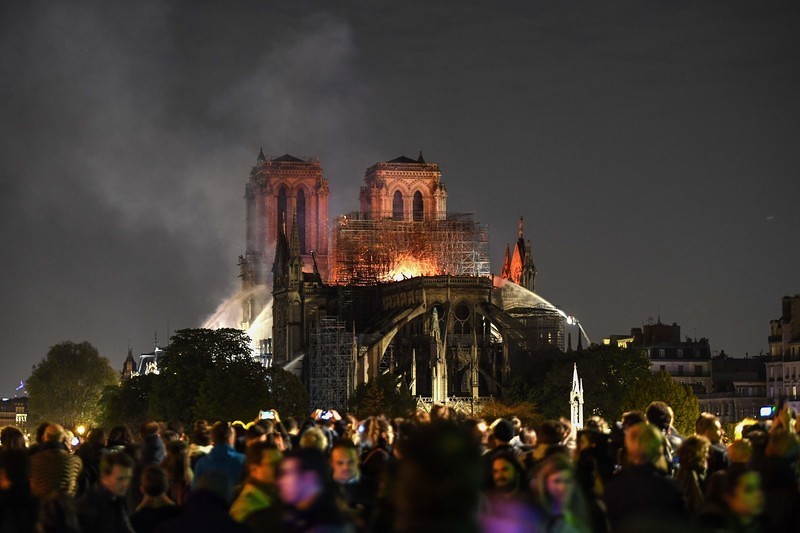 Download von www.picturedesk.com am 15.04.2019 (23:04). Bystanders look on as flames and smoke are seen billowing from the roof at Notre-Dame Cathedral in Paris on April 15, 2019. - A fire broke out at the landmark Notre-Dame Cathedral in central Pa