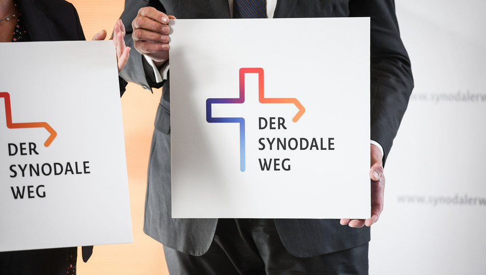 Hände halten ein Schild mit dem Logo zum geplanten Dialog zur Zukunft der katholischen Kirche in Deutschland