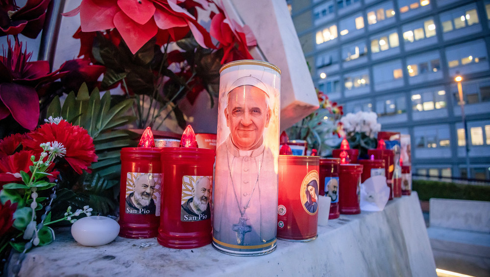 Blumen und Votivkerzen, einige mit dem Abbild von Papst Franziskus, liegen vor dem Gemelli-Krankenhaus in Rom (Italien) am 19. Februar 2025.